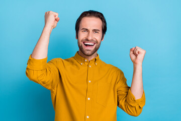 Fototapeta premium Photo of astonished guy raise hands celebrate triumph victory wear yellow shirt isolated blue color background