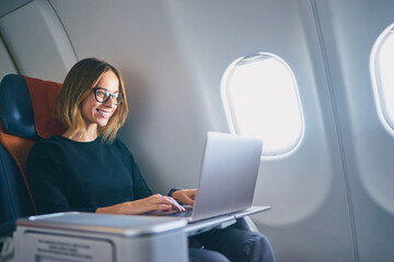 Traveling and technology. Flying at first class. Pretty young businees woman working on laptop...
