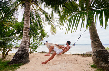 Tropical vacation. Young man relaxing at hammock on tropical beach.