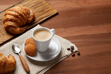 A cup of coffee and a croissant on a wooden table