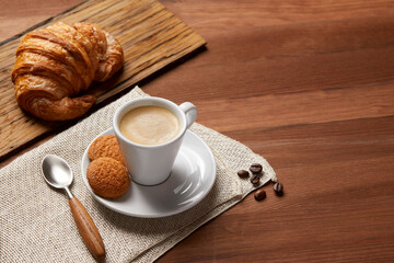 A cup of coffee and a croissant on a wooden table