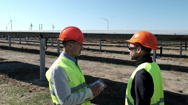 Solar and wind alternative energy. Engineer with tablet gives instructions to worker with sunglasses at electrical substation in countryside