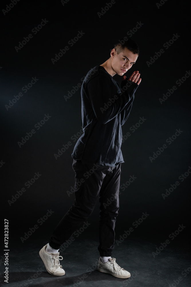 Canvas Prints Full-length picture of an attractive sexy young male model posing isolated on a black background and wearing black blouse and black pants.