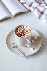 Hot cocoa with marshmallows in ceramic cup with book on grey table. The concept of winter or fall time. Minimal design.