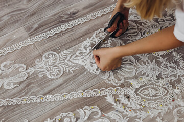 The blond professional tailor is correcting her white ornament for wedding dress.