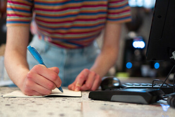 Close up of an unrecognizable bar waitress standing behind the bar counter and writing an order to the notepad.