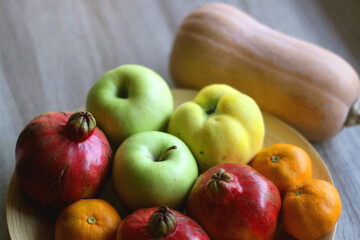 Wooden bowl filled with various seasonal fruit and butternut squash on a table. Selective focus.
