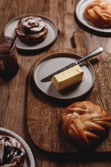 Freshly baked cardamom knot buns (also sweet rolls or swirl buns) with cocoa mug and butter and jam on wooden table. Cosy winter breakfast. Selective focus