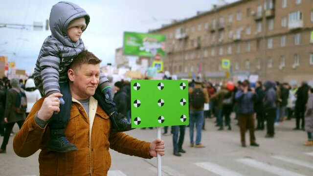 Family of protesting father and son with chroma key space banner. People at political picket demonstration on city streets. Activists with green screen mock up placard. Parent and kid at rally riot.