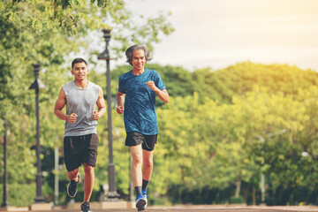 Fototapeta premium Senior elderly man and a young man running together along the walk path in the park. 