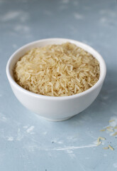 Dry rice in a white bowl on a gray background. Healthy eating concept. Vertical orientation. Rice dishes are cooked in all countries of the world. Popular cereal. Selective focus.