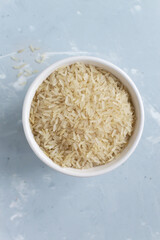 White milled long grain rice in a white bowl on a gray background. Vegetarian food concept. Vertical orientation. Rice dishes are cooked in all countries of the world. Popular cereal. Top view.