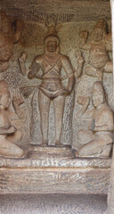 Statue of a Hindu god carved in stone. The rock is located in the background