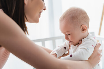 blurred woman smiling while holding baby boy in crib.