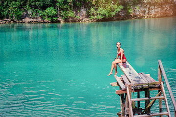 Vacation and activity. Young woman in swimsuit enjoying blue tropical lagoon view sitting on wooden springboard. Siargao Island, Philippines.