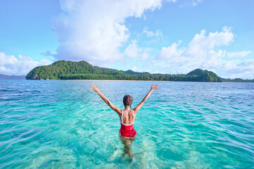 Vacation and freedom. Happy young woman rising hands up standing on tropical beach enjoying beautiful view. © Loginova