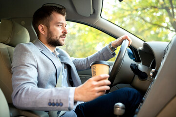 One hand on the steering wheel and other holding a cup of coffee