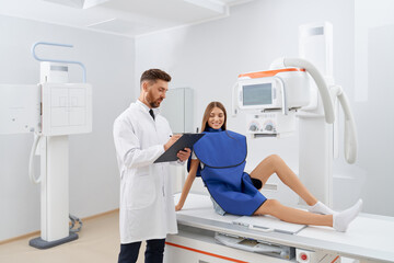 Beautiful young woman wearing blue robe sitting on scanning area on procedure of ultrasound...