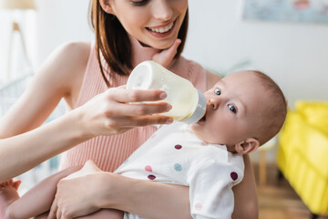 blurred woman smiling while feeding toddler son from baby bottle.