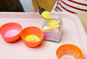 Young children making fun colorful layered granulated wax candles in home by pouring powder in old...