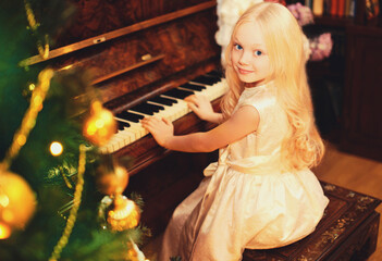 Portrait of little girl child playing on piano at home near christmas tree