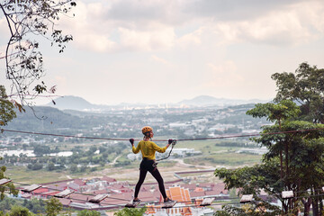 Young woman with climbing gear in an adventure extreme park passing on the high rope road with...