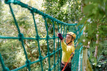 Young woman with climbing gear in an adventure extreme park climbing or passing on the rope road.