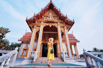 Travel by Asia . Young woman in hat and yellow dress walking near the Chalong buddhist temple on...