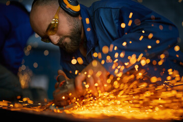 Close up of worker with headphone in dark blue uniform doing gate by electric steel cutter machine...