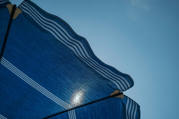 blue sun umbrella on the beach across blue sky and shining sun. Summer vacation background. Copy...