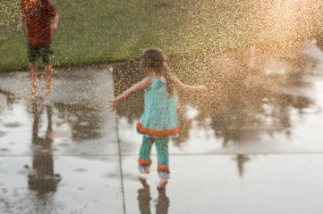 A Kid Child Young Girl Boy Plating in the Rain Water Sprinkler Fun Childhood Unplugged Get Outside Sun Grass Concrete Sunshine 