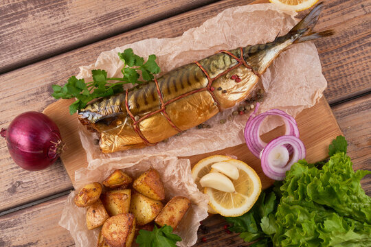 Composition smoked mackerel fish with garnish potatoes lemon greens onions served on wooden board plate top view
