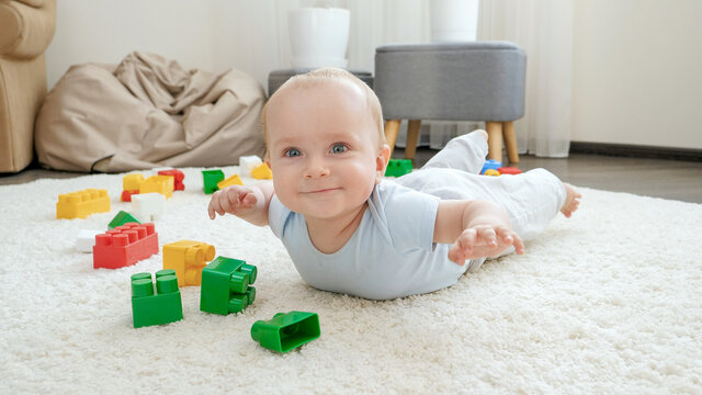 Happy cheerfull baby boy lying on floor next to colorful toys, bricks and blocks at playroom. Concept of children development, sports, education and creativity at home