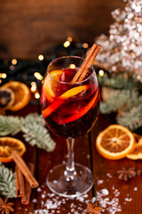 A glass of mulled wine on the wooden table surrounded by Christmas decorations. Festive winter drink vertical photo