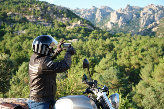 Motorcyclist taking a picture with a smartphone in nature.