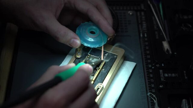 Close up of man microsoldering and repairing a board in a repair shop with solder