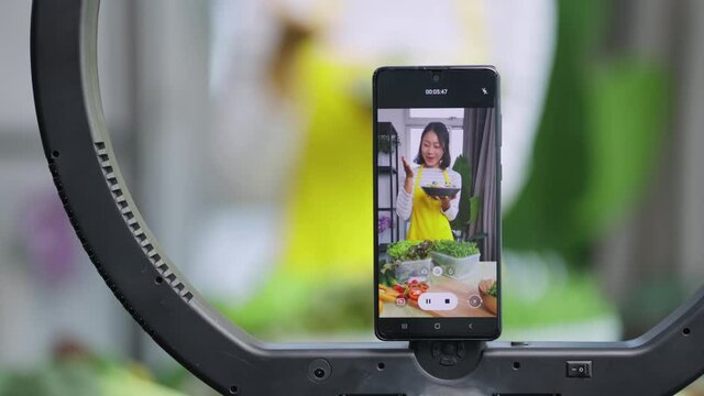 Attractive asian female vlogger lives streaming to all her follower to explain how to make healthy diet salad bowl for moning breakfast meal at home,asian female use smartphone to lives streaming her 