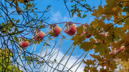 Part of ferris wheel in the park against the blue sky behind trees. Low Angle View Of Ferris Wheel Against blue Sky.