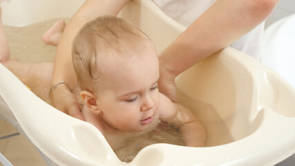 Cute baby boy swimming and washing in small bath at home