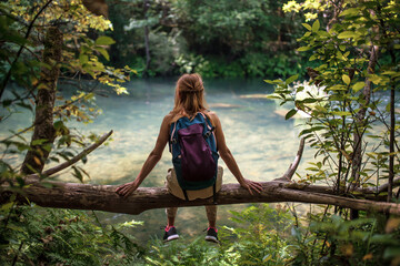 Woman with backpack sitting on trunk of tree in lakeside