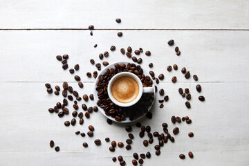 A cup of coffee with coffee beans around it on a white wooden table