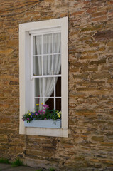 A white-framed window with a flower box set into a brown stone wall.