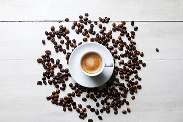 A cup of coffee with coffee beans around it on a white wooden table