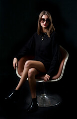 Stylish woman sitting on an armchair over a dark background.