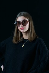 Stylish woman wearing sunglasses looking at camera while posing over a dark background.