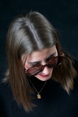 Stylish woman wearing sunglasses and smiling while posing on a dark background.