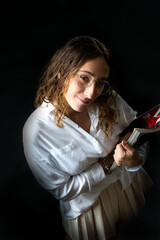 Stylish woman holding fashion magazines while posing on a dark background.