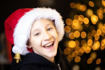 the boy laughs happily and looks into the camera wearing a red Santa Christmas hat