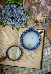 Fototapeta na wymiar Moscow, Russia, June 2010, a cup of milk stands on an open book on a table with notes and a bouquet of forget-me-nots