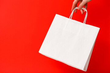 Female hand holding white blank shopping bag isolated on red background. Black friday sale,...